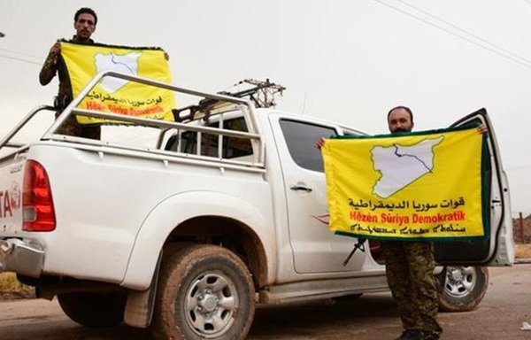 اثنان من المقاتلين يرفعان علم قوات سوريا الديموقراطية في مدينة منبج السورية بعد أن حُررت من قبضة ’الدولة الإسلامية في العراق والشام‘. [حقوق الصورة لحزب الاتحاد السرياني]