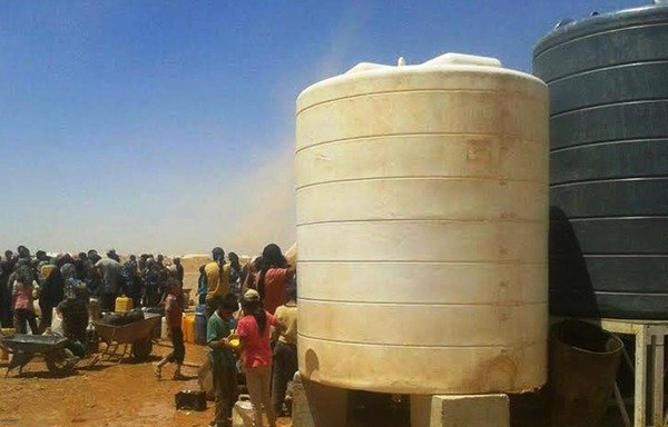 لاجئون سوريون بانتظار الحصول على المياه من صهريج في مخيم الركبان. [حقوق الصورة لصفحة مجلس عشائر تدمر والبادية السورية على فيسبوك]