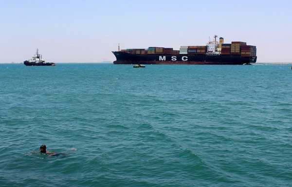 A Yemeni boy swims as a cargo ship passes off the port city of Aden on April 11th. Tensions have flared in Bab al-Mandeb strait since the Houthis attacked a civilian Emirati ship in October. [Saleh al-Obeidi/AFP]