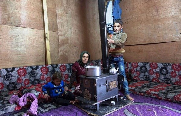 A Syrian woman with her two children huddle around a stove inside their tent in the Bekaa Valley to keep warm. [Photo courtesy of UNHCR]