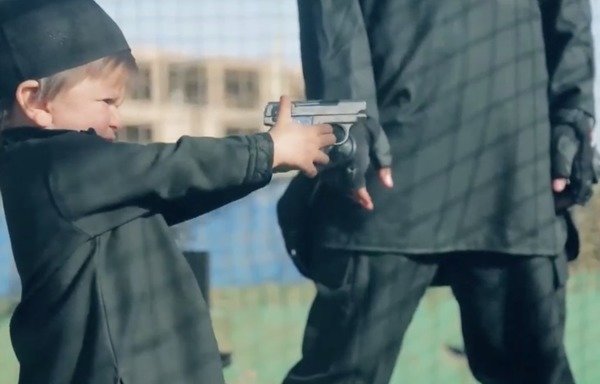 Screen shot from an ISIL video showing a militant giving a toddler a gun. Moments later in the video, the child shoots an 'apostate' to death.