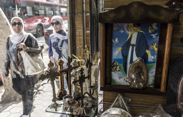 مصريات يسرن أمام مكتبة لبيع المقتنيات المسيحية تعرض صلباناً وصوراً للمسيح وشخصيات دينية قبطية في حي شبرا بشمال القاهرة، يوم 11 نيسان/أبريل [خالد دسوقي/وكالة الصحافة]