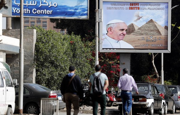 Egyptians walk past a billboard welcoming Pope Francis to Egypt a few hours before the start of his official visit on April 28th. [Thomas Coex/AFP]
