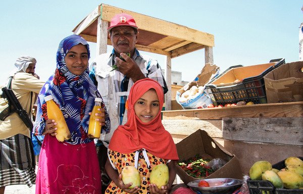 Yemeni girls pose for a picture with mangoes and bottles of juice at a market in the Red Sea port of Mokha on March 17th. The UAE has been sending humanitarian aid to the area. [Saleh al-Obeidi/AFP]