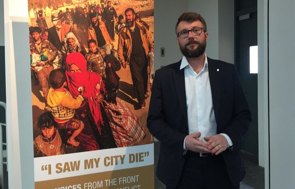 Syria International Committee for the Red Cross communications head Pawel Krzysiek stands beside a poster announcing the 'I Saw My City Die' report, which documents the toll of urban warfare on city residents. [Nohad Topalian/Al-Mashareq]