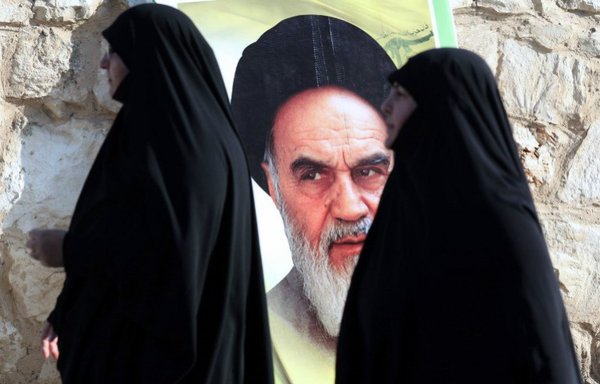 Lebanese women walk past a portrait of the founder of Iran's Islamic Republic, Ayatollah Ruhollah Khomeini, in the southern Lebanese city of Saksakieh, on November 27th, 2015, during the funeral ceremony of Ali Tanana, who was reportedly killed during battles in Syria's Aleppo fighting alongside Lebanon's Shia militia Hizbullah. [Mahmoud Zayyat/AFP]
