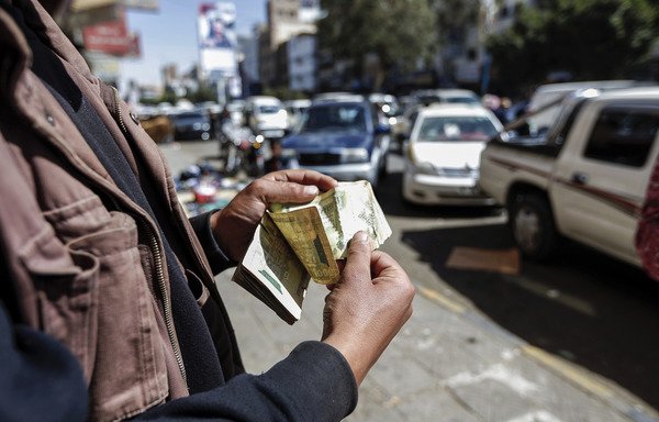 A Yemeni man counts stacks of Yemeni riyals on a street in Sanaa on February 12th. A recent Central Bank decision to float the rate of exchange has met with mixed reactions from bankers. [Mohammed Huwais/AFP]