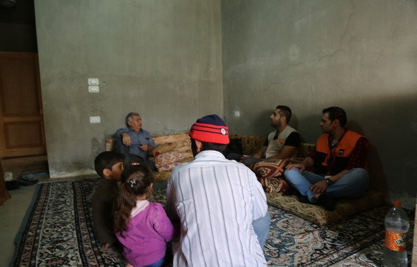 اللاجئ السوري ابو محمد وأطفاله داخل منزله المؤجر حديثاً في اربد مع صاحب المنزل وممثلين عن المجلس النرويجي للاجئين. [حقوق الصورة للمجلس النرويجي للاجئين]