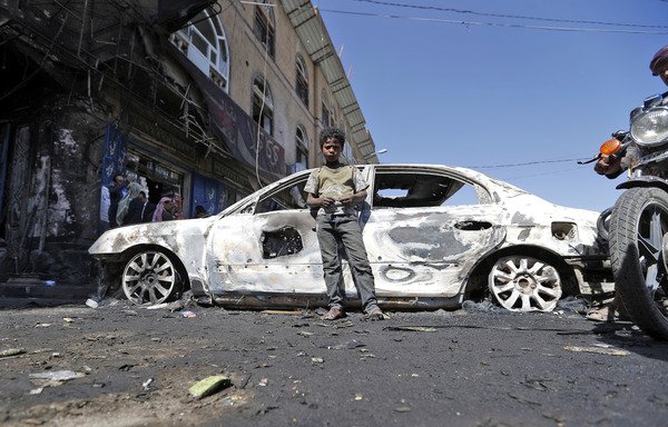 A Yemeni boy stands next to the husk of a burnt car, after recent clashes between the Houthis and loyalists of slain ex-president Ali Abdullah Saleh, in Sanaa on December 6th. [Mohammed Huwais/AFP]
