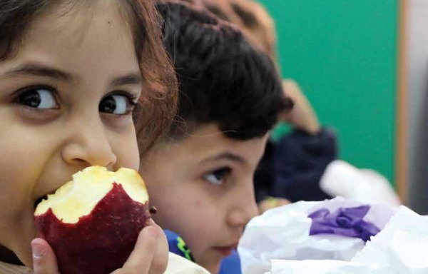 فتاة سورية لاجئة في مدرسة رسمية في لبنان تأكل حصتها اليومية من الفاكهة التي يقدمها برنامج الأغذية العالمي لأهالي الأطفال الذين يرتادون المدارس الرسمية. [حقوق الصورة لبرنامج الأغذية العالمي]