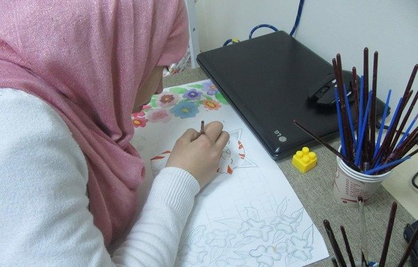 اللاجئة السورية المقيمة في الأردن بتول البيطار، ترسم لوحة خلال فصل للعلاج بالفن في مركز السير بوبي تشارلتون في عمان. [حقوق الصورة لمنظمة آسيا للتدريب التنموي]