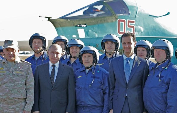 Russian President Vladimir Putin, his Syrian counterpart Bashar al-Assad, and Russian Defence Minister Sergei Shoigu (L) pose with Russian air force pilots during their visit to the Russian air base in Hmeimim in the Syrian province of Latakia on December 11th. [Mikhail Klimentyev/Pool/AFP]