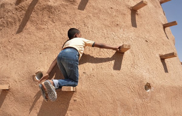 A child climbs on the outside walls of a newly-constructed beehive classroom in Jordan's Zaatari village. [Photo courtesy of Martina Rubino/EAHR]