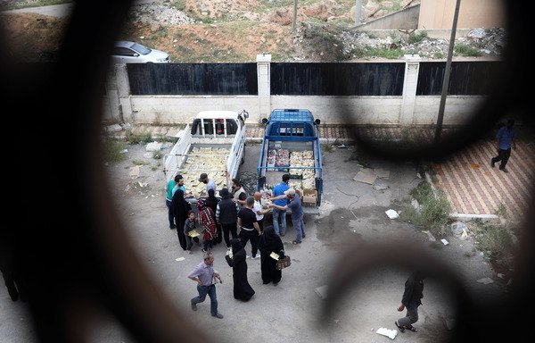 Workers distribute iftar meals to impoverished families, who fled their homes in the former opposition enclave of Eastern Ghouta, at a school in Idlib on May 19th. [Omar Haj Kadour/AFP]
