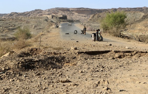 Yemeni men stand in a damaged road following an airstrike on the northwestern province of Saada, a stronghold of the Houthis, on January 24th. [STRINGER/AFP]