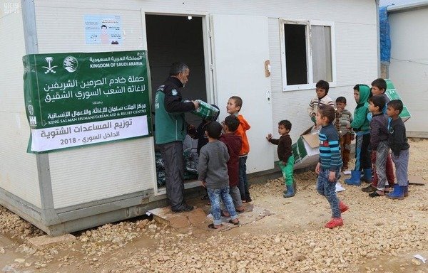 A King Salman Humanitarian Aid and Relief Centre worker distributes winter assistance to children inside Syria. [Photo courtesy of the Saudi Press Agency]