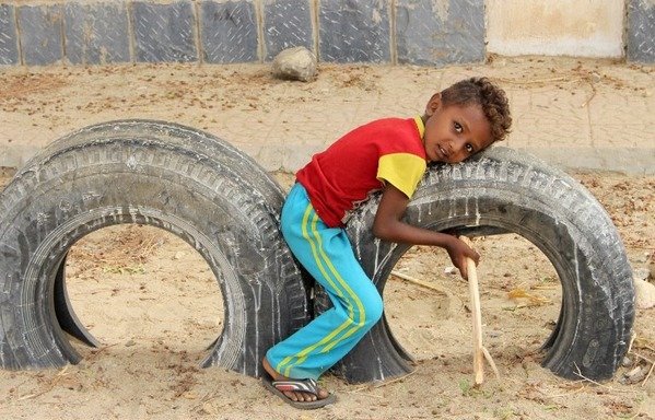 A Yemeni child plays on used car tires as displaced people from al-Hodeidah receive humanitarian aid donated by a Turkish NGO in the northern Yemeni district of Hajjah province on August 6th, 2018. [Essa Ahmed/AFP]
