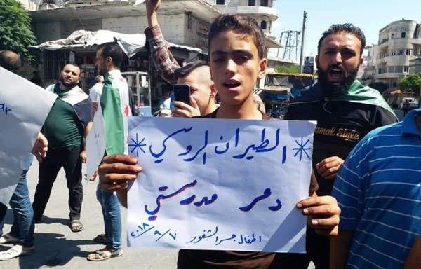 A boy holds a banner accusing Russian warplanes of destroying his school during a demonstration in Jisr al-Shughur on September 7th. [Photo courtesy of Syria Civil Defence]