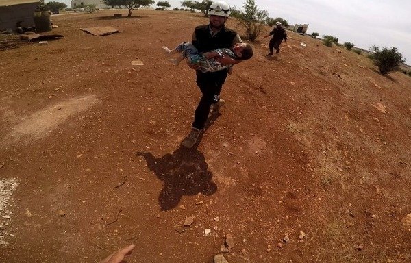 A Syria Civil Defence member rescues a child who was injured in the regime bombing of Idlib. [Photo courtesy of Syria Civil Defence]