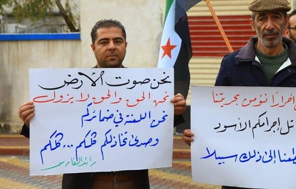 Residents of Kafr Nabl hold signs denouncing the assassination of activists Raed al-Faris and Hammoud Junaid, who opposed Tahrir al-Sham and were killed November 23rd. [Photo courtesy of Haisam al-Idlibi]