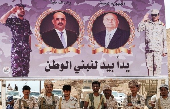 A picture taken on August 8th, 2018 shows Yemeni soldiers loyal to the government standing below a banner showing President Abd Rabbu Mansour Hadi (R) and Interior Minister Ahmed al-Maysari as they attend a graduation of new police cadets in the south-eastern port city of al-Mukalla, in the first such ceremony after the city was retaken from al-Qaeda. [Karim Sahib/AFP] 