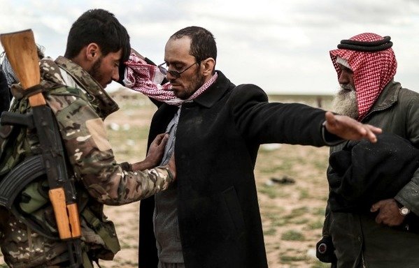 Men suspected of being ISIS elements are searched by a member of the Syrian Democratic Forces (SDF) after leaving ISIS's last holdout of al-Baghouz, in Syria's northern Deir Ezzor province on February 27th. [Delil Souleiman/AFP]