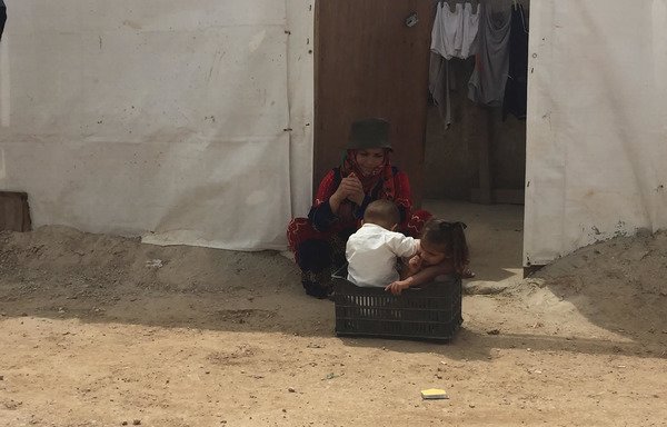 A Syrian woman watches her children play outside a tent in Bar Elias refugee camp in Lebanon. [Nohad Topalian/Al-Mashareq]
