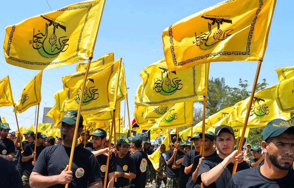 Members of the Iran-backed Iraqi militia Harakat al-Nujaba raise the militia's flag during a parade. [Photo circulated on social media]