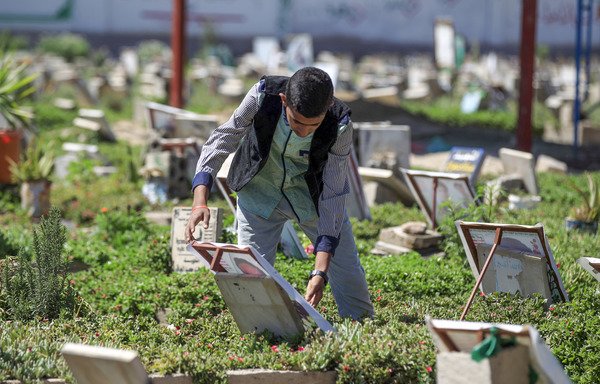 A Yemeni boy fixes a portrait of a deceased person in a cemetery in Sanaa on March 25th. [Mohammed Huwais/AFP]