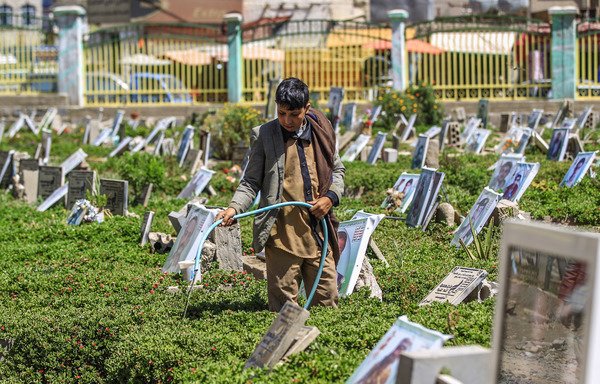 A Yemeni boy waters plants and cleans tombstones in a Sanaa cemetery on March 25th. [Mohammed Huwais/AFP]
