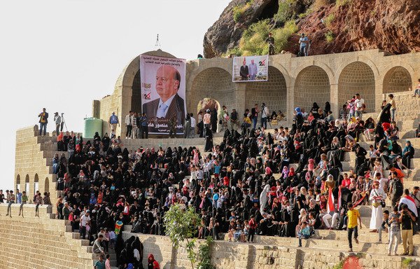 Yemenis wave national flags near a banner of President Abd Rabbu Mansour Hadi during a celebration marking the 56th anniversary of the 1962 revolution which established the Yemeni republic, in al-Qahira citadel outside Taez on September 23rd, 2018. [Ahmad al-Basha/AFP]