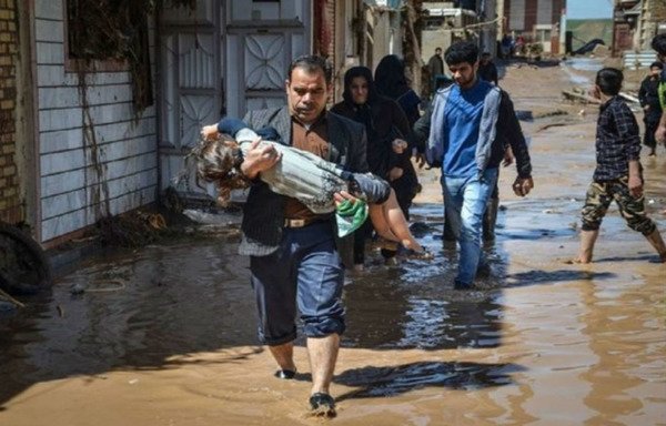 An Iranian man carries a child through a flooded street in the aftermath of April's torrential rains. [Photo circulated on social media]