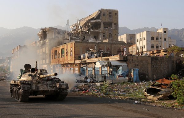رزمندگان یمنی وفادار به رییس جمهوری در تبعید یمن، عبد منصور ربه هادی، سوار بر تانک از کنار ساختمانی که طی نبرد با حوثی های مورد حمایت ایران در شهر تعز، ویران شده در روز 30 مه می گذرند. [احمد الباشا/خبرگزاری فرانسه]