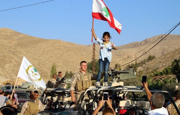 A girl scout waves a national flag next to a Lebanese Army soldier on a military vehicle, during a celebration of the soldiers' return from battling ISIS on the country's eastern front bordering with Syria, in the eastern town of Ras Baalbek on August 30th, 2017. [Stringer/AFP]