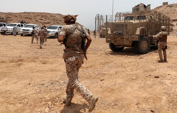 A picture taken August 8th, 2018 during a trip in Yemen organised by the UAE's National Media Council shows a Yemeni soldier walking past Emirati armoured vehicles near the Hadramaut provincial capital of al-Mukalla. [Karim Sahib/AFP]