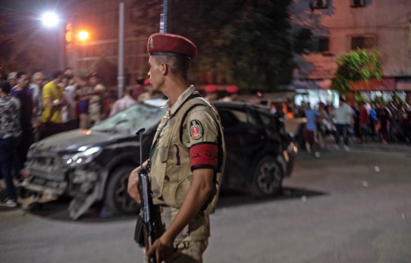 A member of the Egyptian forces stands guard as onlookers gather on August 5th at the scene of a deadly explosion outside the National Cancer Institute in Cairo. [Aly Fahim/AFP]