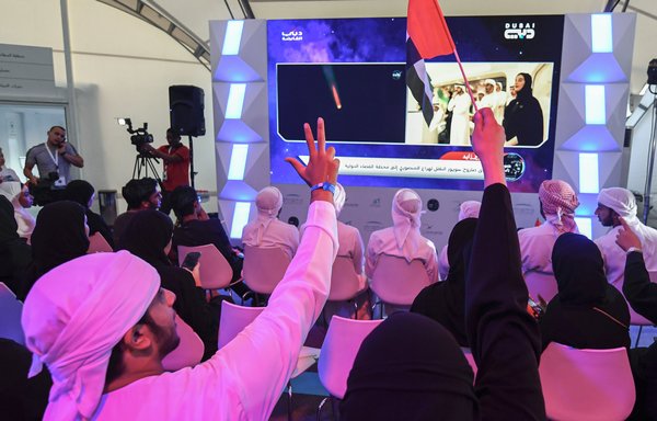 People raise three fingers signifying "win, victory and love" and wave Emirati national flags as they watch screens showing the Soyuz MS-15 spacecraft lifting off from Baikonur Cosmodrome in Kazakhstan carrying 35-year-old Emirati astronaut Hazzaa al-Mansoori, who spent eight days aboard the International Space Station, at Mohammed Bin Rashid Space Centre in Dubai on September 25th. [Karim Sahib/AFP]
