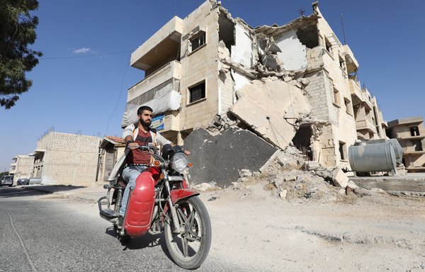 المباني التي تعرضت للقصف تشكل خلفية حياة المعري. وهنا يمر بدراجته عبر شارع مدمر بمعرة النعمان. [عمر الحاج قدور/وكالة الصحافة الفرنسية]