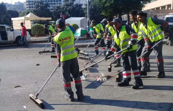 A group of cleaners sweep Riad al-Solh Square on Wednesday morning (October 30th). The remaining tents set up by protesters can be seen behind them. [Nohad Topalian/Al-Mashareq]