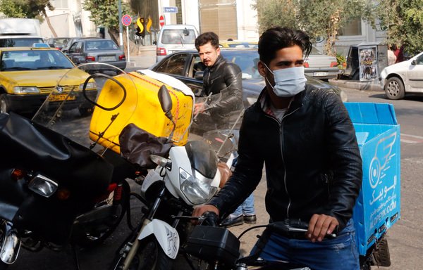 An Iranian man covers his face with a mask against pollution as he walks through a main avenue in central Tehran on November 7th. [Stringer/AFP]
