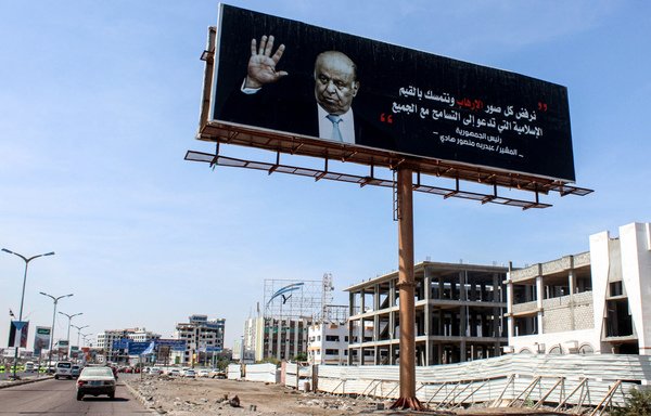 A car drives past a huge billboard bearing a portrait of Yemeni President Abd Rabbu Mansour Hadi on a main road in the port city of Aden. [Saleh al-Obeidi/AFP]