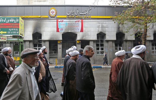 Iranians walk past the branch of a local bank that was damaged during demonstrations against gasoline price hikes on November 20th in Shahriar, west of Tehran. [Atta Kenare/AFP]