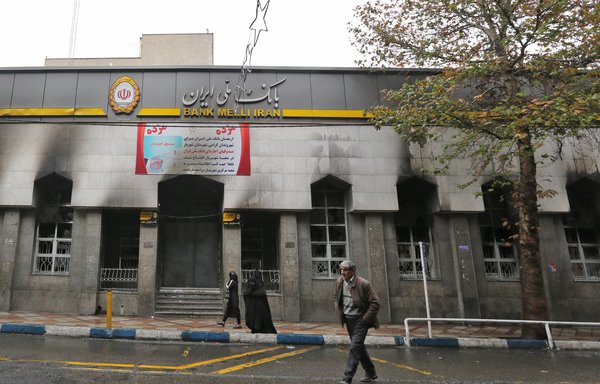 Iranians walk past the branch of a local bank that was damaged during demonstrations against gasoline price hikes, on November 20th in Shahriar, west of Tehran. [Atta Kenare/AFP] 
