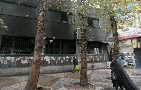An Iranian woman walks past the branch of a local bank that was damaged during demonstrations against gas price hikes on November 20th in Shahriar, west of Tehran. [Atta Kenare/AFP]