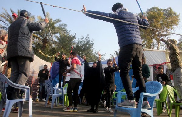 Iraqi anti-government protestors flash the victory sign outside their protest tents in Baghdad's Tahrir Square following news of the killing of IRGC top commander Qassem Soleimani. [Stringer/AFP]