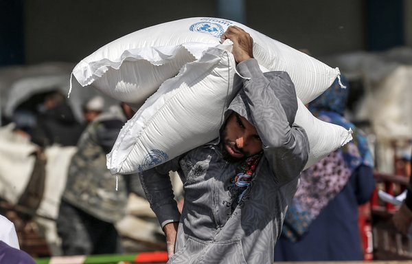 A Palestinian man carries on his shoulder a sack of flour received from a UN Relief and Works Agency (UNRWA) distribution centre in the southern Gaza Strip refugee camp of Rafah, on November 17th. [Said Khatib/AFP]