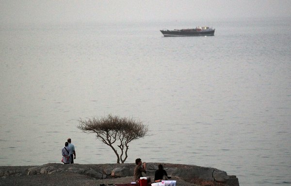 People sit along the coast line overlooking the Strait of Hormuz off Oman in this file photo from March 13th, 2012. [Karim Sahib/AFP]