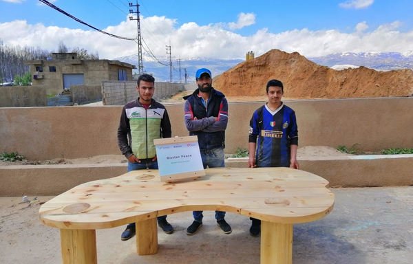 شباب لاجئون يقفون خلف طاولة خشبية أنشأوها في إطار برنامج تدريب ماستر بيس للنجارة. [حقوق الصورة لمنظمة سوا للإغاثة والتنمية]