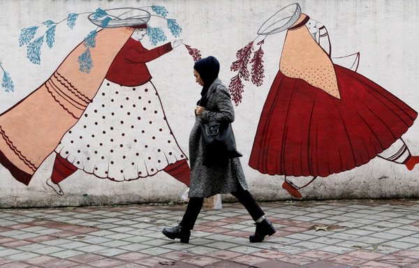 An Iranian woman walks past an artistic mural in Tehran on November 19th. More than 40 years after the 1979 Islamic Revolution, Iranians have yet to see the positive changes they were promised. [Atta Kenare/AFP]