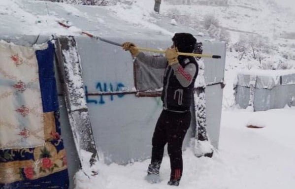 لاجئ سوري يزيل الثلج عن شادر خيمة بلاستيكي في مخيم بالقرب من عرسال. [حقوق الصورة للجنة صوت اللاجئ السوري في لبنان على فيسبوك]